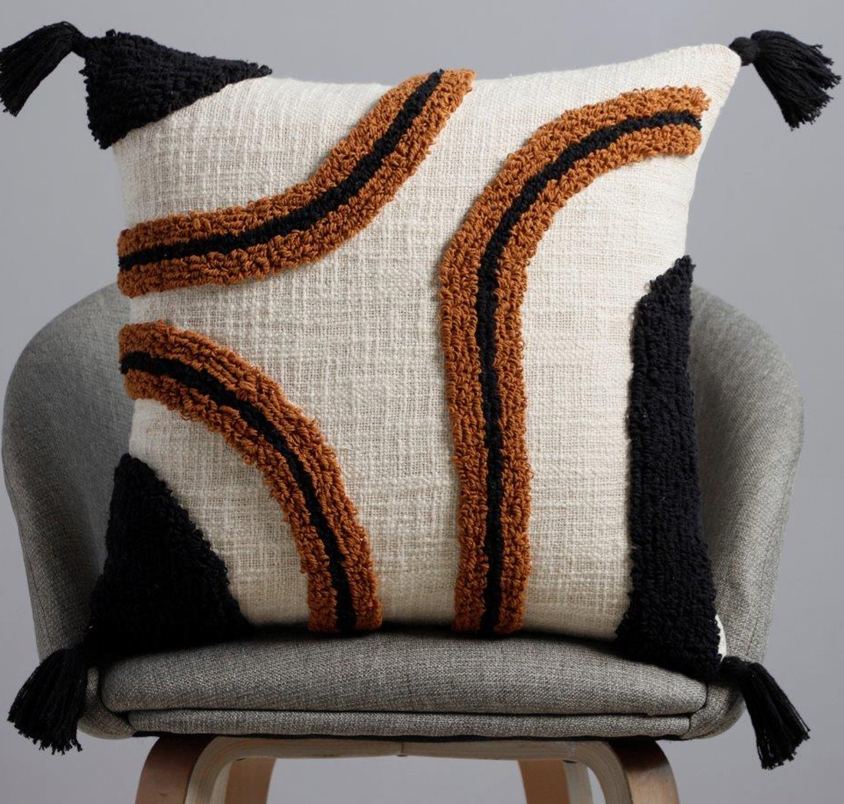 Ivory cotton cushion with amber rust tufted arc and black abstract design with black tassels